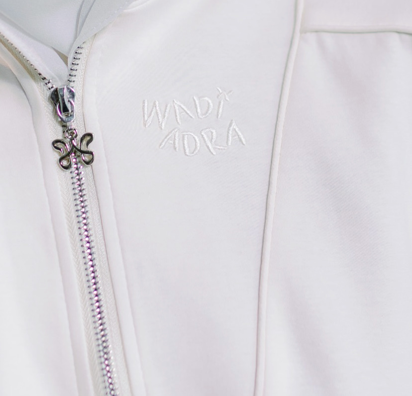 Embroidered Wadi Adra wordmark with monogram zipper pull on ivory garment